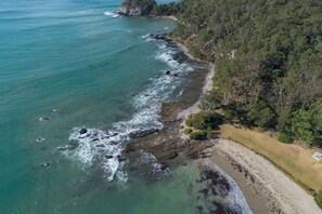 An aerial view of a coastal area with a beach, rocky shoreline, and dense forest.