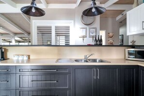 A modern kitchen with a double sink, dark cabinetry, pendant lighting, and a window with blinds.