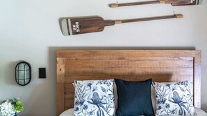 A bedroom with a wooden headboard, two pillows with floral patterns, and a wall-mounted wooden object. - Secluded 3-Bed Retreat Moments to the Beach (Surf Beach)