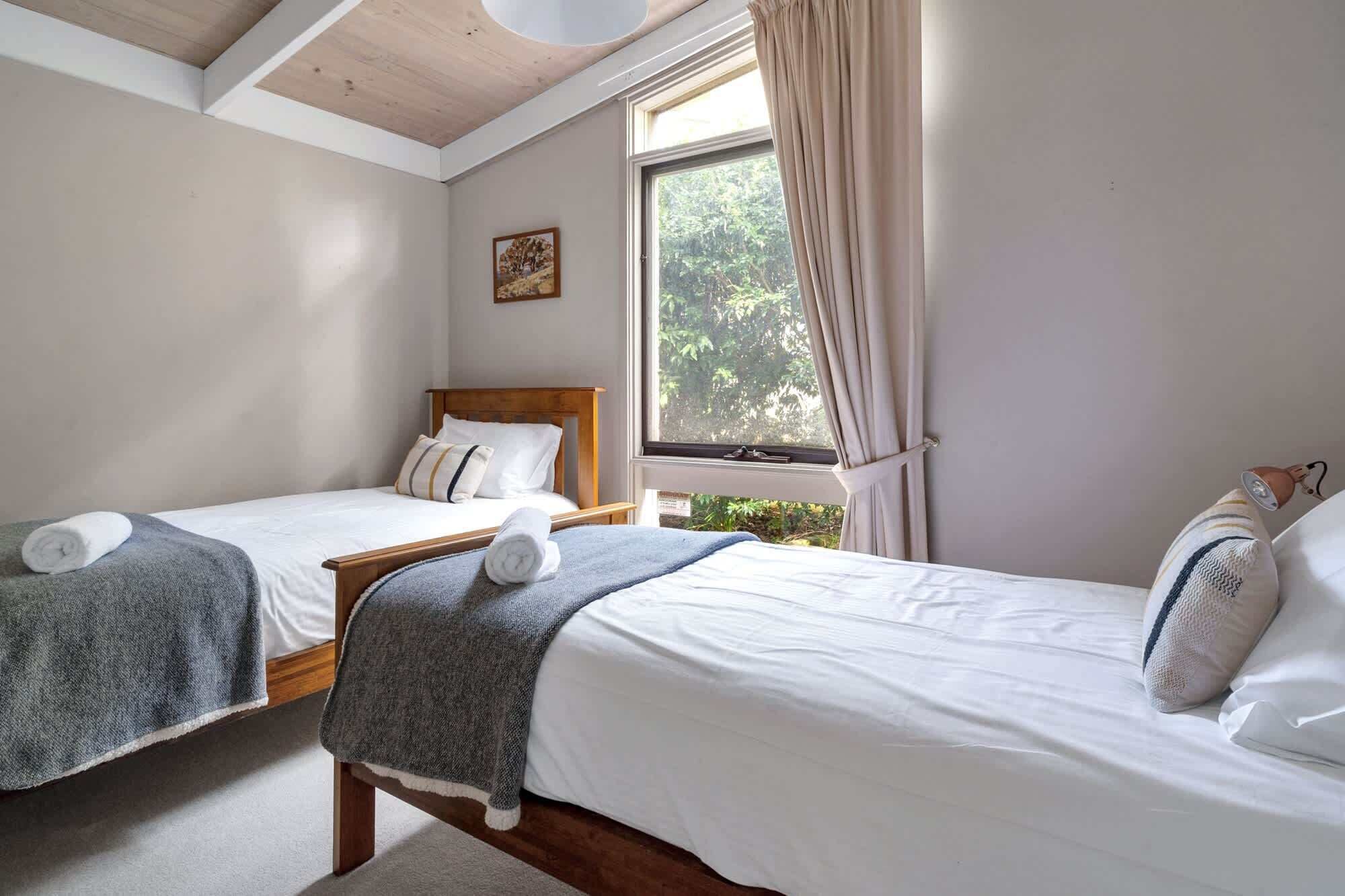 Une chambre avec deux lits, une fenêtre avec des rideaux, un plafond en bois et une petite table.
