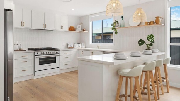 Een moderne keuken met witte kasten, een centraal eiland met barstoelen, een ingebouwde oven en hanglampen.