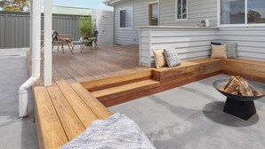 Een overdekt terras met houten banken, een vuurkorf en een zithoek met kussens.