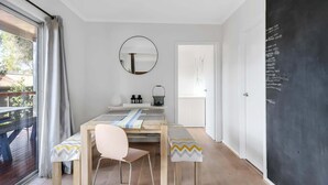 A modern room with a wooden dining table, a round mirror, and a chalkboard with writing. - Cosy Getaway with Fireplace and Spacious Backyard (Broulee)