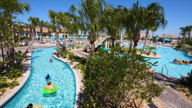 A resort pool area with multiple swimming pools, palm trees, and lounge chairs. - 1580 Champions Gate (Davenport)