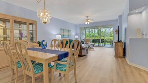 A spacious dining area with a wooden table and chairs, a chandelier, and a view of the outdoors through large sliding glass doors. - 23516 Sandycreek Terrace 205 (Bonita Springs)