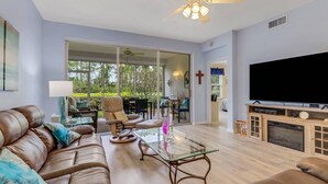 A living room with a leather couch, a glass coffee table, a TV, and a fireplace. - 23516 Sandycreek Terrace 205 (Bonita Springs)