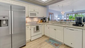 A modern kitchen with white cabinetry, a stainless steel refrigerator, a microwave, and a coffee maker. - 23516 Sandycreek Terrace 205 (Bonita Springs)