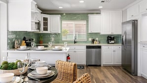 A modern kitchen with white cabinets, a stainless steel refrigerator, and a dining area with a round table and wicker chairs. - The Palm & Putt: Heated Pool | Golden Tee | Bocce (Phoenix)
