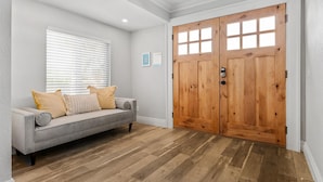 A room with a grey sofa, wooden flooring, and a wooden double door. - The Palm & Putt: Heated Pool | Golden Tee | Bocce (Phoenix)