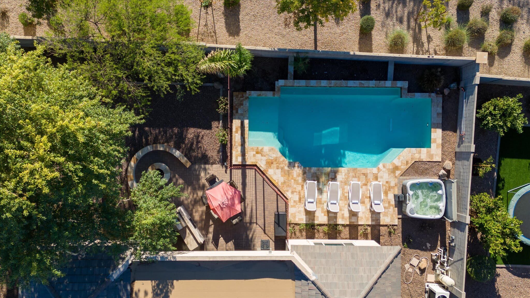 An aerial view of a swimming pool area with a hot tub, lounge chairs, and a staircase leading to a deck.