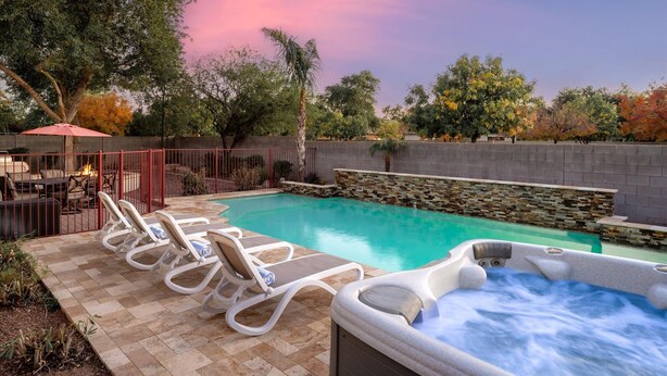 A swimming pool with lounge chairs and a hot tub, surrounded by stone walls and trees. - Backyard Oasis | Pool, Theater & Fire Pit (Glendale)