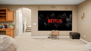 A home entertainment room with a large flat-screen TV mounted on the wall, a wooden cabinet, a desk with a computer, and a comfortable seating area. - Backyard Oasis | Pool, Theater & Fire Pit (Glendale)