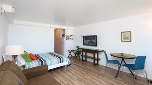 Une chambre d’hôtel de taille réduite, comprenant un lit, un bureau avec une chaise, une télévision et une petite table à manger.