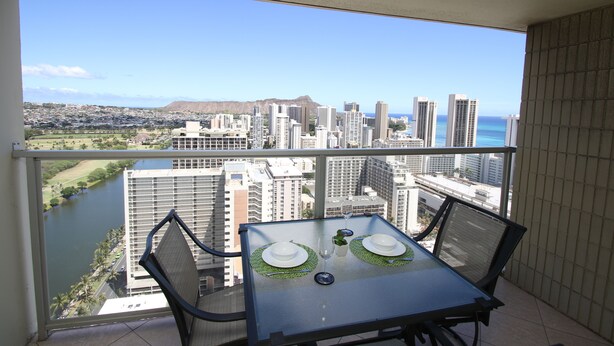 Un balcon avec une table dressée pour deux personnes, offrant une vue sur le paysage urbain et une rivière.