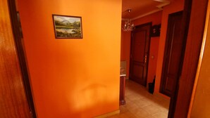 Un couloir aux murs orange et au sol carrelé, qui mène à une porte près d’un radiateur et d’une poubelle.