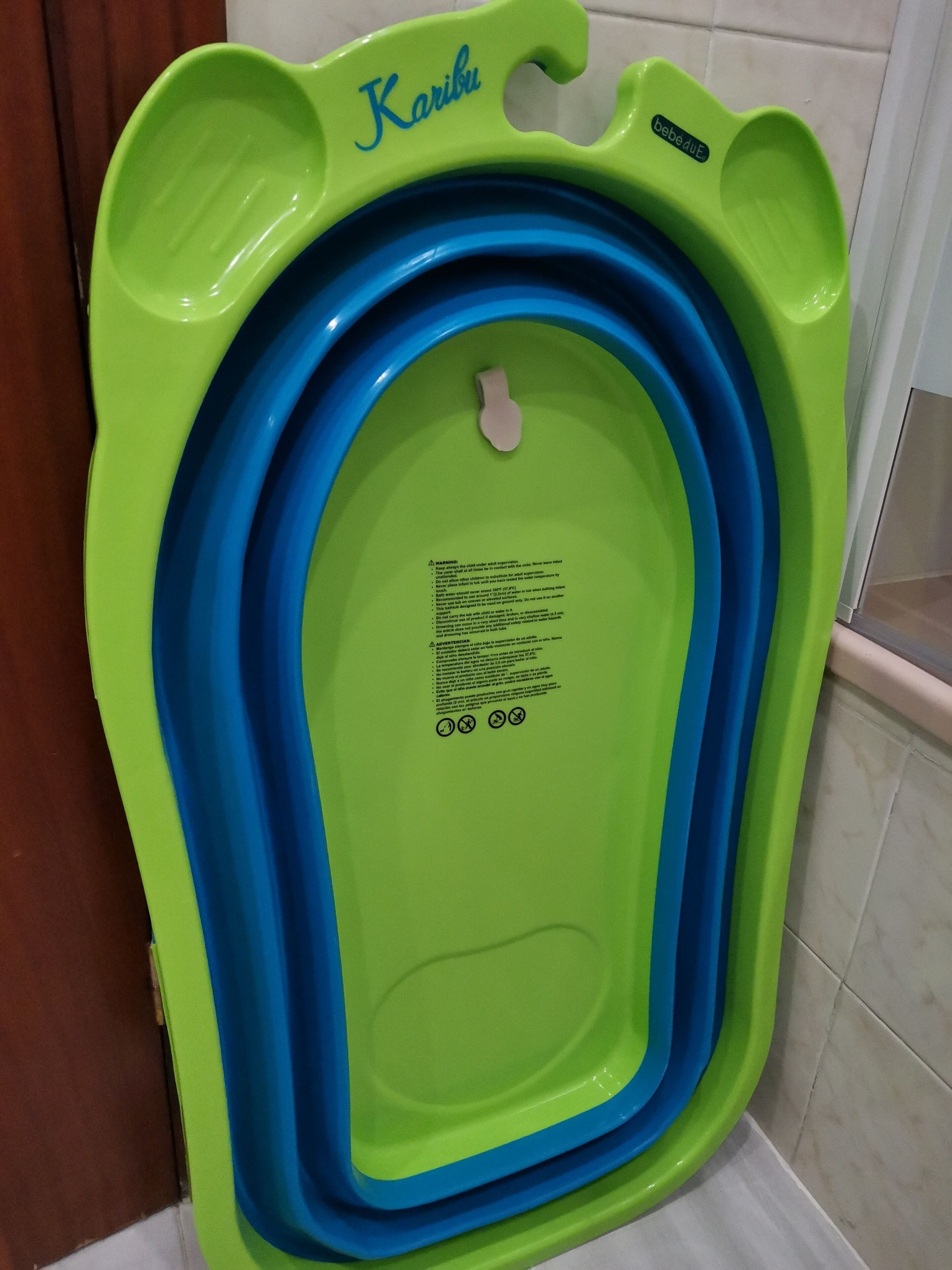 A green and blue baby bathtub with a label and safety instructions.