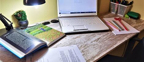 Taula amb un ordinador portàtil, llibre obert, papers, làmpada, petita planta en test i material de papereria.