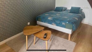 A bedroom with a bed, a small wooden table, and a remote control on the table. - Studio Hypercentre Orléans, Entre Bord de Loire et Cathédrale (Orléans)