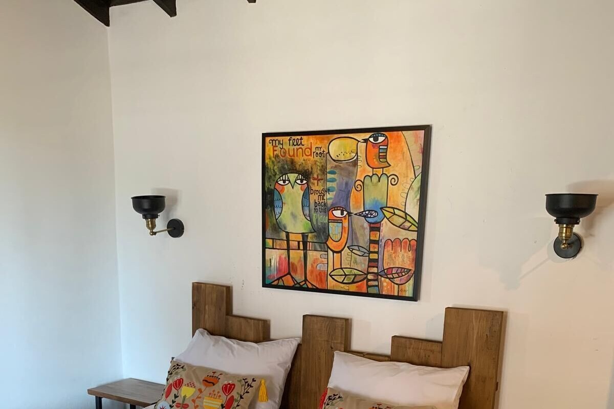 A bedroom with a bed, two nightstands, a wall-mounted lamp, and a colorful abstract painting.