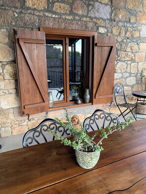 A rustic stone wall with a wooden door and window shutters. A potted plant with green leaves is on a wooden table. - Chakra (Ayvacik)