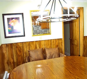 A dining area with a round wooden table, two brown cushioned benches, a framed abstract painting, and a decorative metal ceiling fixture.