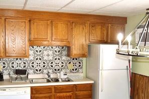 A kitchen with wooden cabinets, a stainless steel sink, a white refrigerator, and patterned backsplash tiles.