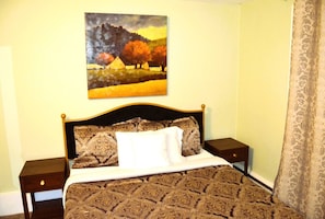 A neatly made bed with patterned bedding, a headboard, two bedside tables, and a painting of a landscape on the wall.
