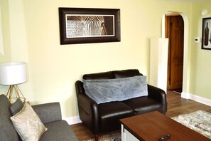 Een woonkamer met een leren bank, een houten salontafel, een grijze bank en een lamp.