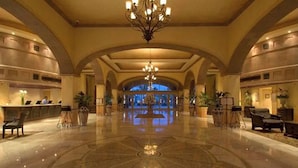 A spacious lobby with a central chandelier, arched ceiling, and a reception desk.