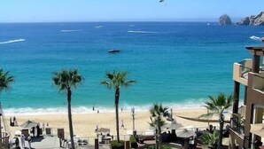 A beach view with a clear sky, palm trees, and a distant rocky outcrop.