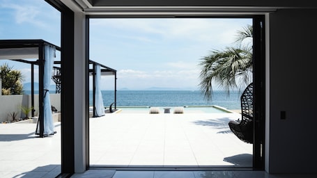 A modern outdoor patio with a pool, lounge chairs, and a view of the sea.