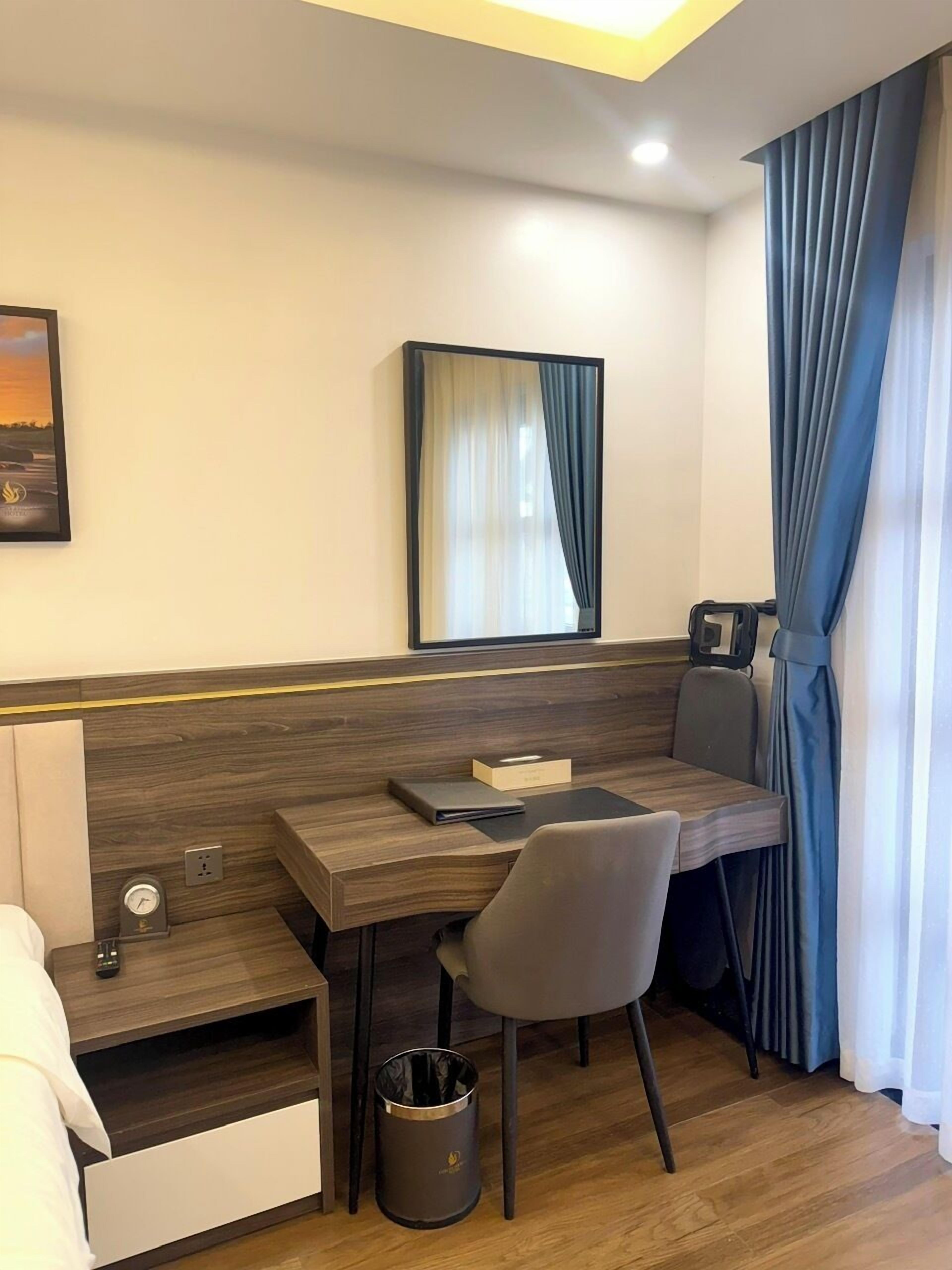 Una habitación de hotel moderna con un escritorio de madera, una silla, un cesto de basura pequeño y una cama.