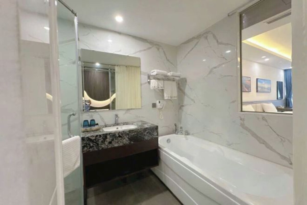 Un baño moderno con pared de mármol, un espejo grande, una bañera y un lavabo con tocador.