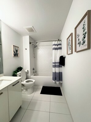 A modern bathroom with a toilet, sink, and bathtub. There are framed botanical prints on the wall. - Miami Highrise with Rooftop Pool and Gym (Miami)