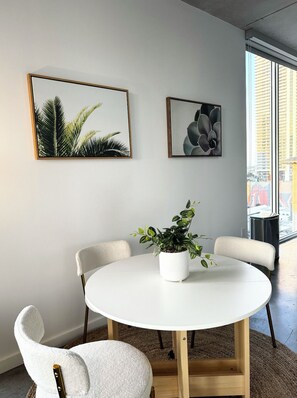 A round white table with four white chairs, a potted plant, and two framed artworks on the wall. - Miami Highrise with Rooftop Pool and Gym (Miami)