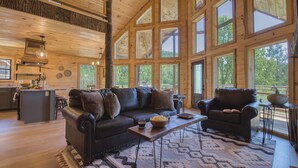 A spacious living area with a large wooden ceiling, a leather sofa, a coffee table, and a view of the outdoors through large windows. - Private Indoor Pool + Hot Tub + Sauna + Theater + Game Room | Mins to Gatlinburg (Gatlinburg)