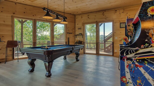 Una mesa de billar en una habitación con paredes de madera y ventanas amplias.