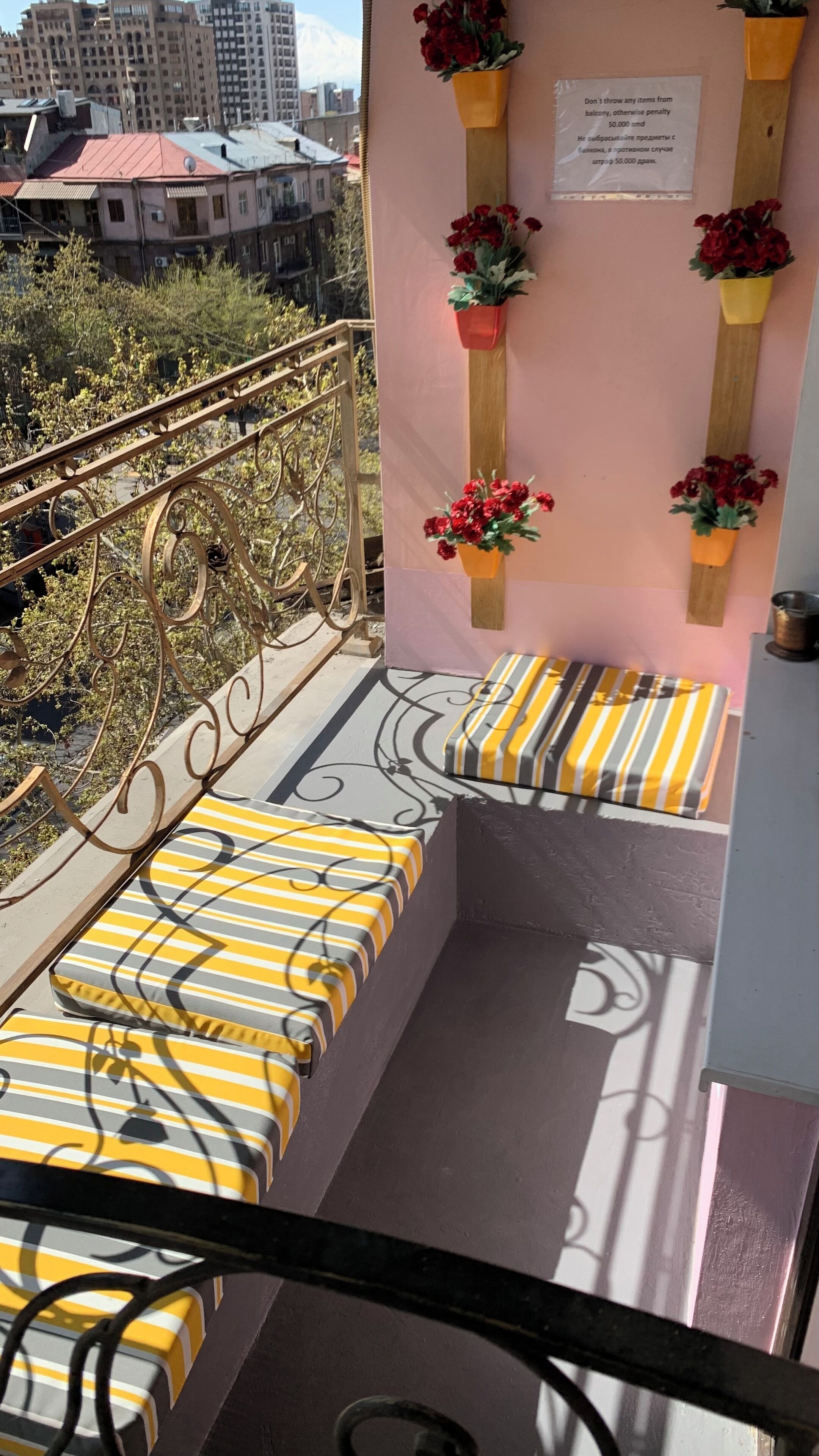 A balcony with yellow-striped cushions, a metal railing, and red flowers in pots.