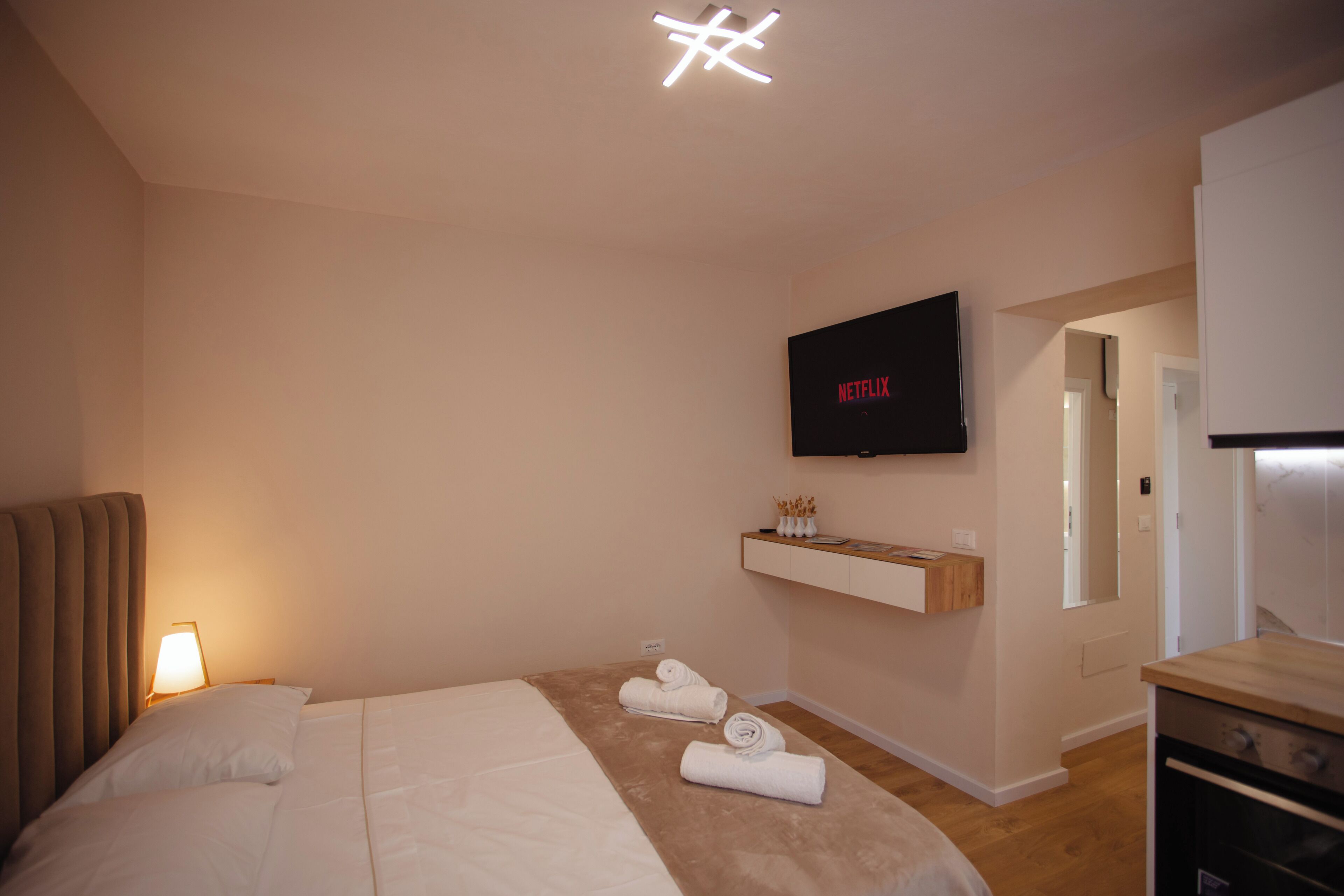 Ein Hotelzimmer mit einem Bett, einem an der Wand befestigten Fernseher, einem Holzschrank und einer Tür zu einem weiteren Raum.