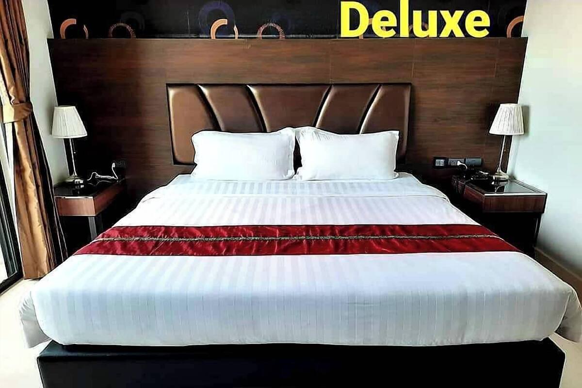A large bed with a wooden headboard, two bedside tables with lamps, and a red throw blanket.