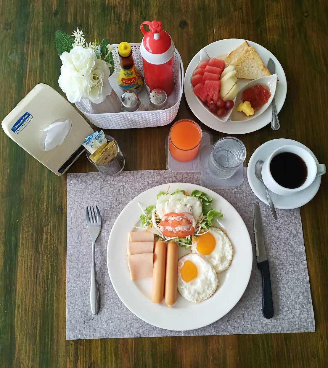 A breakfast setting with a plate of eggs, ham, and vegetables, a cup of coffee, and a tray with condiments and a teapot.