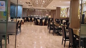 A modern dining area with a high ceiling and reflective floor, featuring multiple tables and chairs arranged for dining. - Constancy Jomtien Pattaya Hotel (Sattahip)