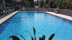 A rectangular swimming pool with a clear blue water surface, surrounded by a wooden deck and potted plants. - Constancy Jomtien Pattaya Hotel (Sattahip)