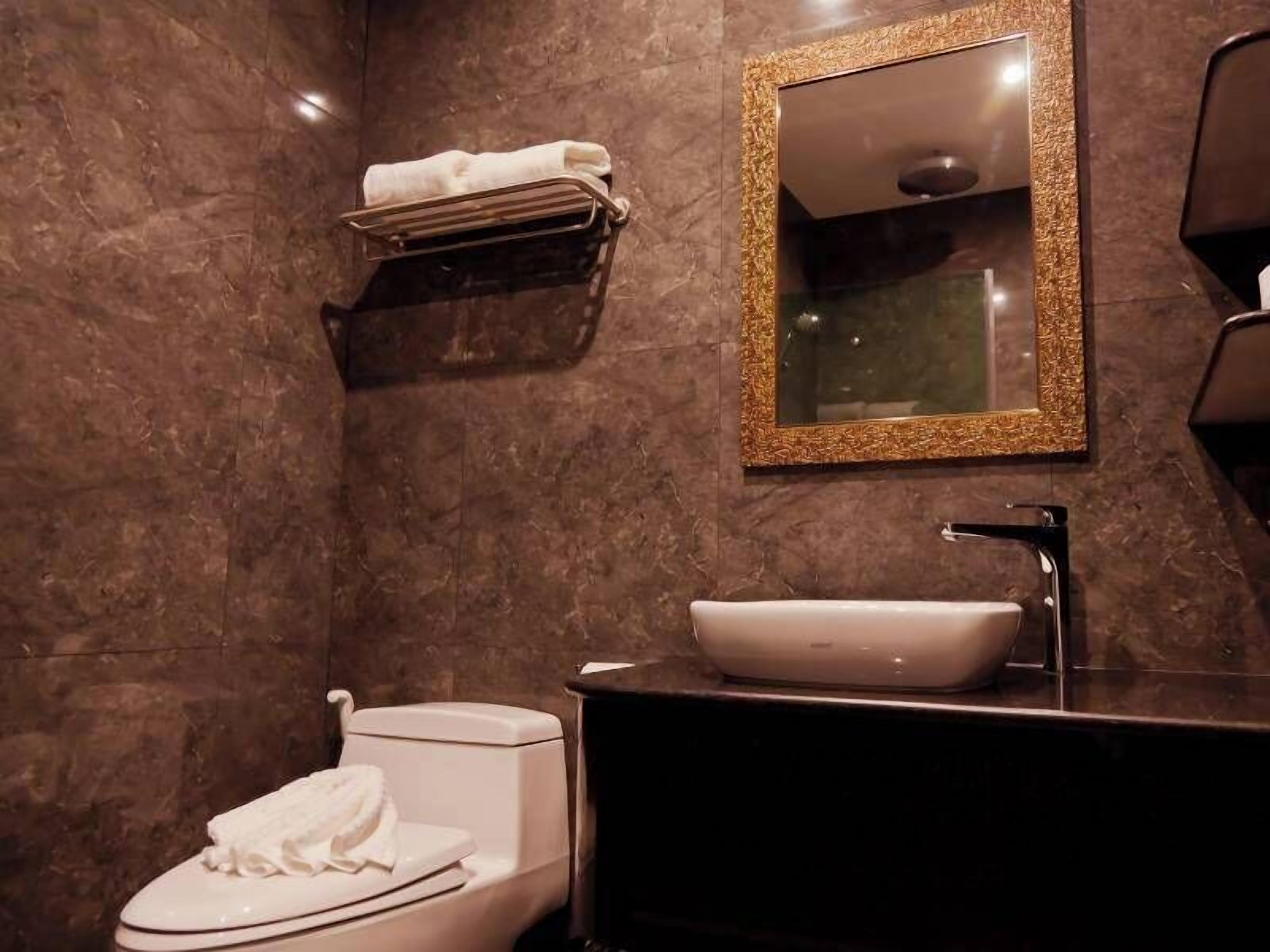 A modern bathroom with a marble wall, a white toilet, a black sink with a white basin, and a gold-framed mirror.