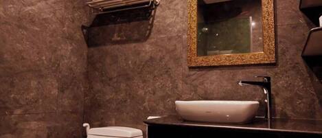 A modern bathroom with a marble wall, a white toilet, a black sink with a white basin, and a gold-framed mirror.