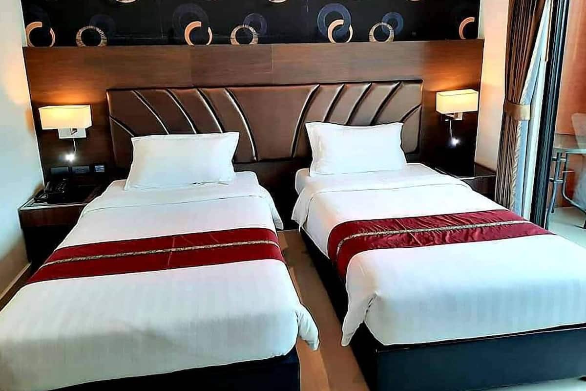 A hotel room with two beds, each with white linens and red accents, a wooden headboard, and bedside lamps.