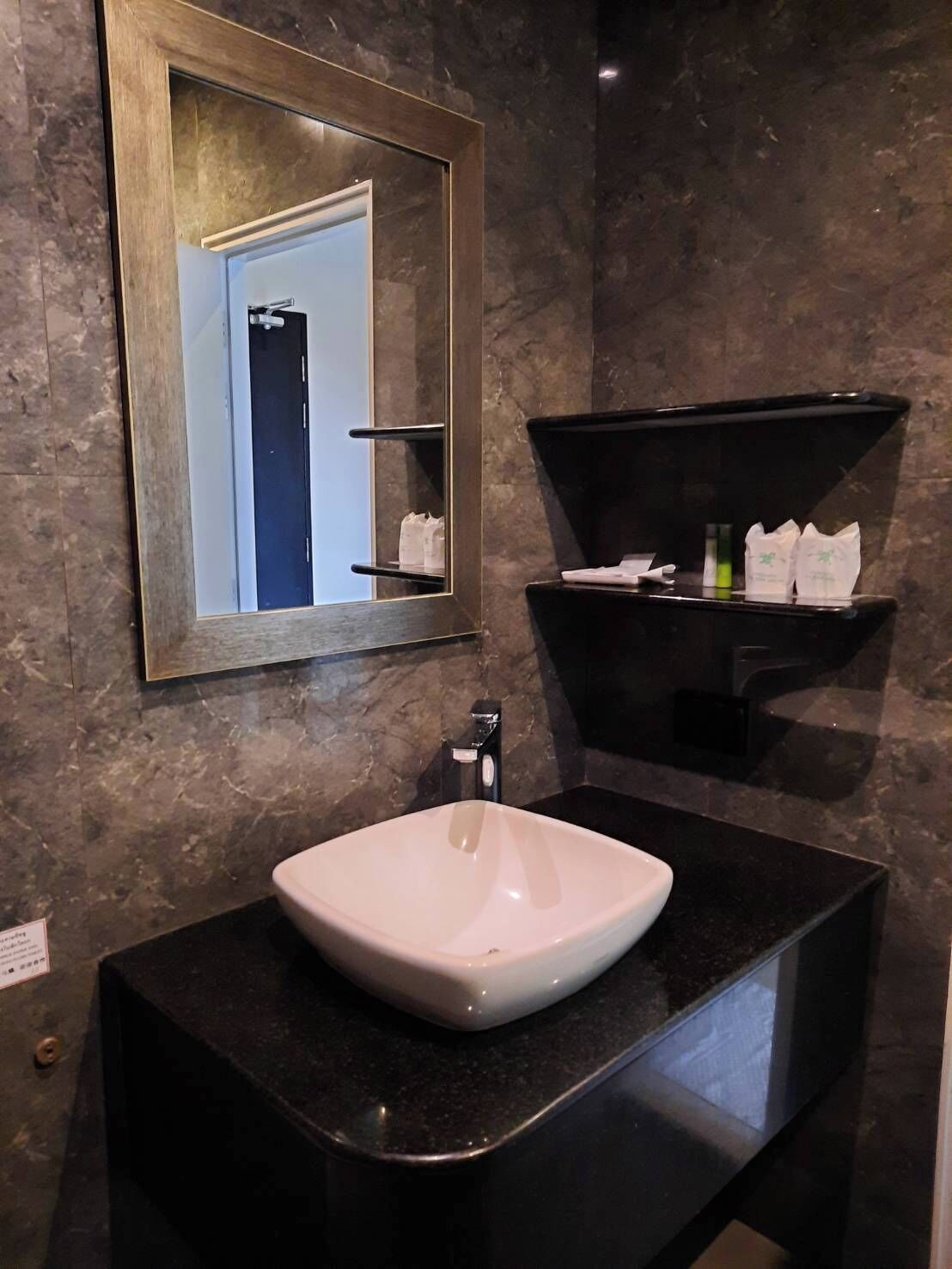 A bathroom with a white sink, a mirror, and a black shelf with toiletries.