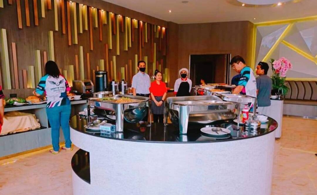 A buffet area with multiple serving stations, a central counter, and a modern interior design with vertical wooden slats on the wall.