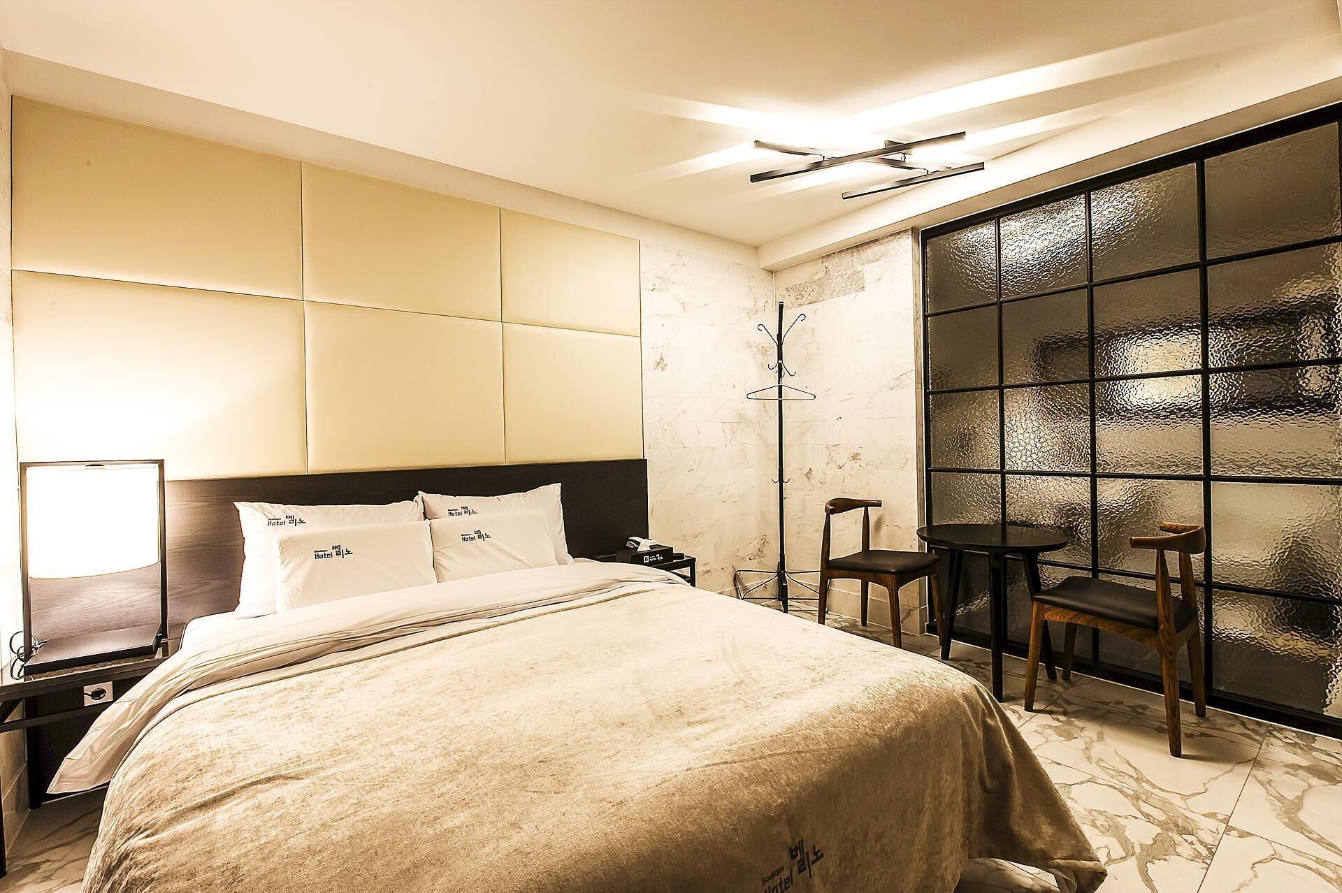 A hotel room with a bed, a bedside table, a chair, a small table, and a large window with a view.