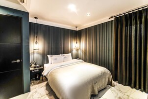 Un dormitorio moderno con una cama grande, paredes revestidas en paneles oscuros y dos lámparas fijadas a la pared.